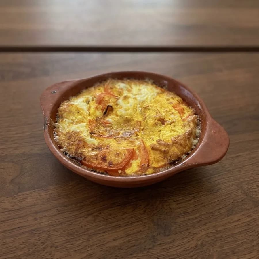 Eggs and tomato baked in a red clay fukhar dish, set golden on top, on a wooden table